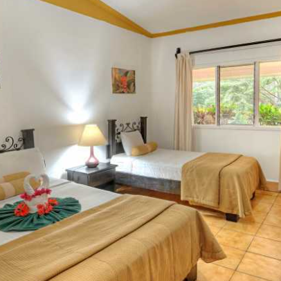 Ein helles Hotelzimmer mit zwei Betten, dekoriert mit Blumen und einem Nachttisch mit einer Lampe.