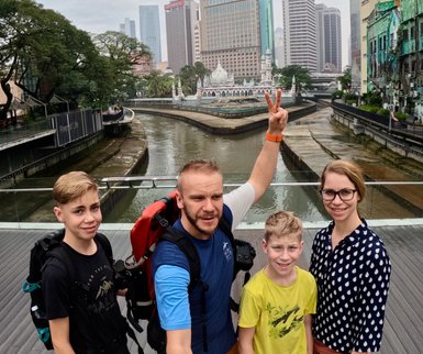 Familie posiert fröhlich für ein Selfie an der Flussmündung mit der Masjid Jamek im Hintergrund – Malaysia & Borneo Reise mit Kindern