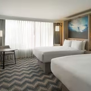 Ein modernes Hotelzimmer mit zwei Betten, großen Fenstern und einem stilvollen Teppichmuster, das eine entspannende Atmosphäre schafft.