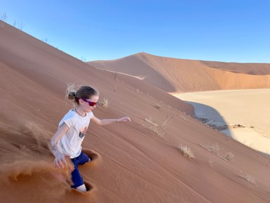 Ein Mädchen saust eine Sanddüne hinunter - Namibia Urlaub mit Kindern