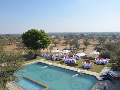 Ein Blick auf den Pool des Hotels Mandawa Haveli, umgeben von eleganten Tischen und Sonnenschirmen im Freien.