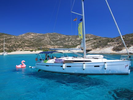 Ein Segelboot schaukelt sanft auf dem klaren, blauen Wasser, während ein pinker Flamingo-Schwimmring daneben schwimmt.