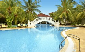 Ein malerischer Pool mit einer eleganten weißen Brücke, umgeben von üppigen Palmen und Sonnenliegen, strahlt tropisches Flair aus.