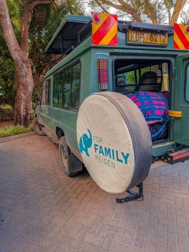 Ein grünes Safari-Fahrzeug steht auf einem gepflasterten Weg, umgeben von üppigem Grün und Bäumen.