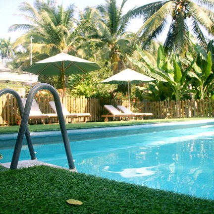 Ein einladender Pool umgeben von üppigem Grün und Palmen, mit Liegen und Sonnenschirmen im Hintergrund.