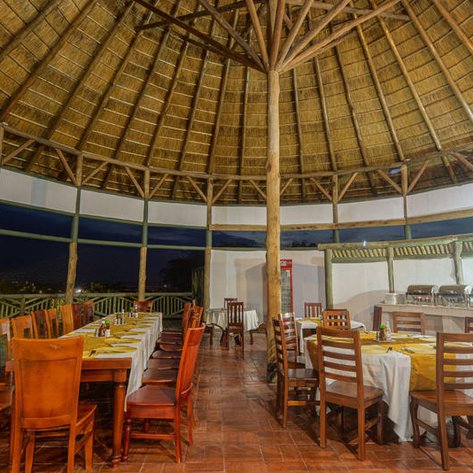 Der Speisesaal im Tilenga Safari Lodge zeigt eine einladende Atmosphäre mit Holzmöbeln und einem hohen Strohdach.