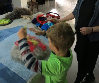 Ein Junge in einem grünen T-Shirt arbeitet mit buntem Filzmaterial, während eine Frau ihm aufmerksam zuschaut.