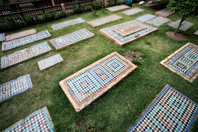 Bunte Mosaikplatten liegen verstreut auf dem Gras, umgeben von Pflanzen und einer friedlichen Atmosphäre.