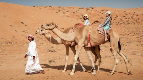 Beduine führt zwei Kamele mit zwei Mädchen durch die Wüste – Oman Familienreise