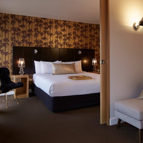 Ein stilvolles Hotelzimmer mit einem großen Bett, goldenen Akzenten und einer Palmenmuster-Tapete im Hintergrund.