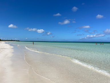Ein ruhiger Strand mit feinem, weißen Sand und klarem, türkisfarbenem Wasser unter einem strahlend blauen Himmel.
