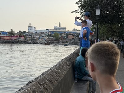 Am Ufer des Wassers stehen Kinder und Erwachsene, während ein Junge mit einem Handy die Aussicht fotografiert.