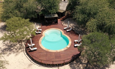 Ein runder Pool mit sanften Stufen ist von einer Holzterrasse und Liegen umgeben, umgeben von Bäumen in einer ruhigen Umgebung.