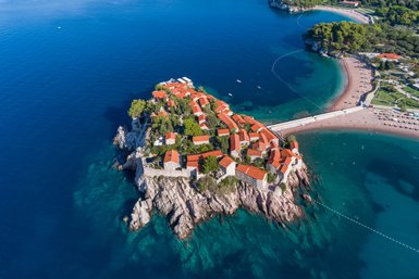 Eine malerische Küstenansicht zeigt eine kleine Insel mit roten Dächern und umgeben von klarem, blauem Wasser.