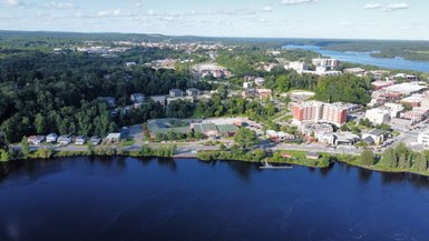 Eine Luftaufnahme zeigt eine Stadtlandschaft mit einem ruhigen Fluss, umgeben von Bäumen und modernen Gebäuden.