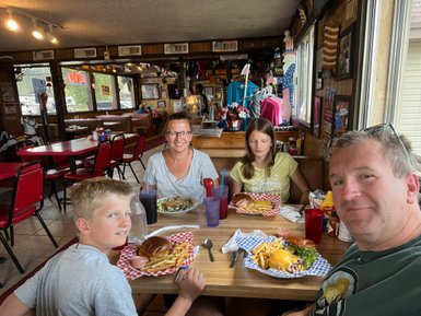 Eine Familie genießt ein entspanntes Essen in einem Diner, umgeben von rustikalem Dekor und bunten Stühlen.