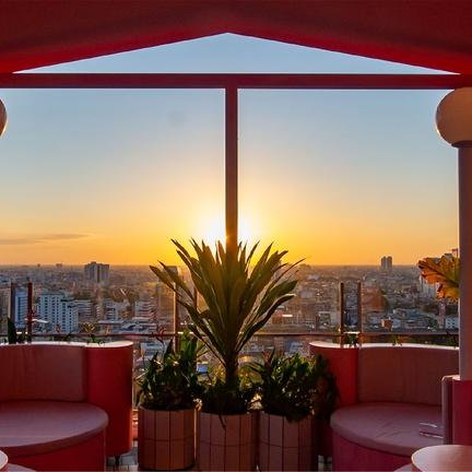 Ein sonniger Abendblick über die Stadt Bangkok von einer stilvollen Terrasse mit pinkfarbenen Möbeln und grünen Pflanzen.