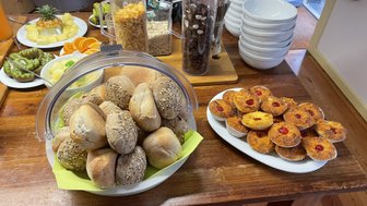 Ein reichhaltiges Frühstücksbuffet mit frischen Brötchen, Obst und süßen Leckereien auf einem Holztisch angerichtet.