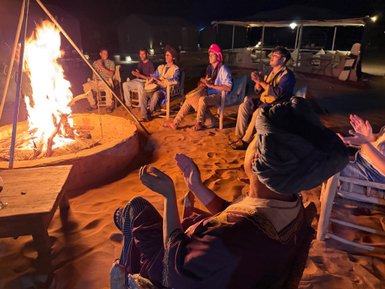 Umgeben von einem lodernden Lagerfeuer sitzen Menschen in einer Wüstenlandschaft und genießen die Nacht.