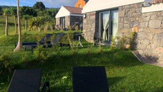 Zwei Liegen stehen auf dem grünen Rasen vor einem modernen Steinhaus mit großen Fenstern und einer hellen Fassade.