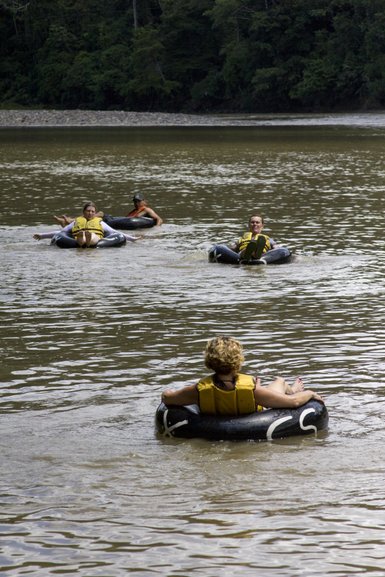 Fünf Personen treiben entspannt auf Reifen in einem ruhigen Fluss, umgeben von üppigem Grün und einem friedlichen Ambiente.