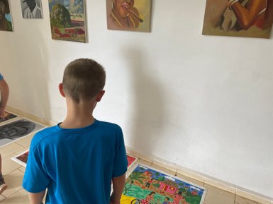 Ein Junge in einem blauen T-Shirt betrachtet aufmerksam farbenfrohe Kunstwerke auf dem Boden eines hellen Raumes.