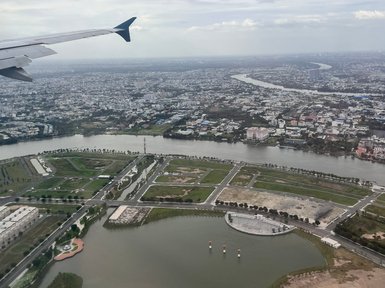 Der Blick aus dem Flugzeug zeigt eine weitläufige Stadtlandschaft mit einem Fluss, der sich durch die grüne Umgebung schlängelt.