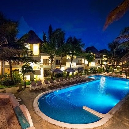 Ein beleuchteter Pool in einem Hotel, umgeben von Palmen und Liegen, strahlt eine entspannte Urlaubsatmosphäre aus.