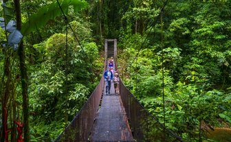 Eine Familie überquert eine Hängebrücke inmitten üppiger, grüner Vegetation in Costa Rica.