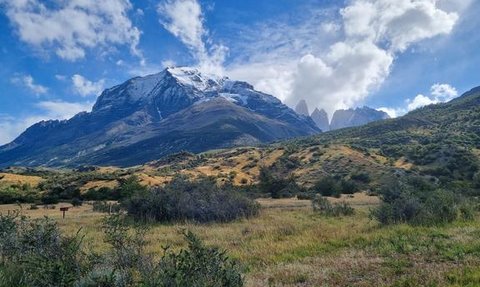 Majestätische Berge mit schneebedeckten Gipfeln erheben sich über eine grüne, hügelige Landschaft unter einem strahlend blauen Himmel.