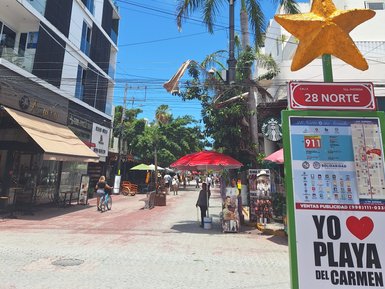 Eine belebte Straße in Playa del Carmen mit bunten Schirmen und einem großen, goldenen Stern auf einem Schild.
