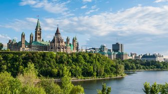 Die beeindruckende Parlamentsgebäude von Ottawa erhebt sich majestätisch über den grünen Hügel, umgeben von strahlend blauem Himmel.