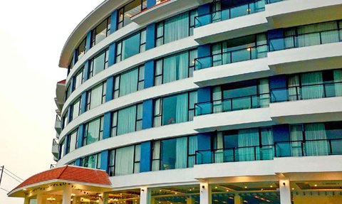 Ein modernes Hotelgebäude mit großen Fenstern und einem geschwungenen Design, umgeben von Bäumen und einer ruhigen Umgebung.
