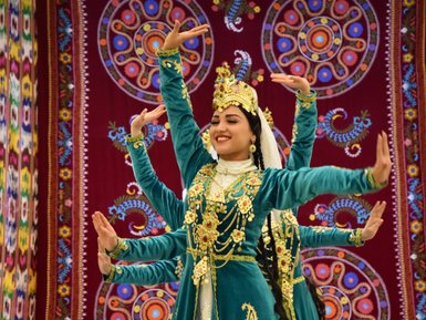 Eine Tänzerin in traditioneller Kleidung lächelt, während sie mit anmutigen Bewegungen auf einer Bühne tanzt.