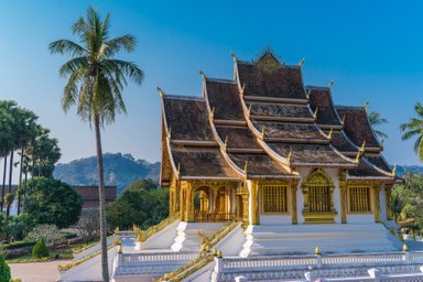 Ein prächtiger Tempel mit goldenen Verzierungen und einem klaren blauen Himmel im Hintergrund, umgeben von Palmen.