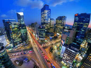 Die Stadt Seoul erstrahlt in der Dämmerung, mit leuchtenden Wolkenkratzern und lebhaften Straßen voller Autos.