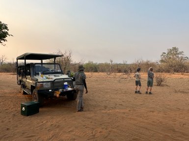 Ein Geländewagen steht auf sandigem Boden, während zwei Kinder in der Ferne die Umgebung beobachten.