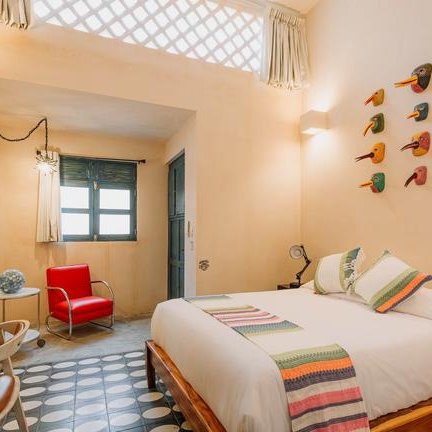 Ein helles Zimmer mit einem großen Bett, bunten Wanddekorationen und einem roten Sessel, der einladend wirkt.