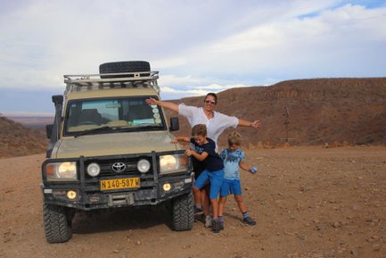 Eine Mutter steht mit ihren beiden Söhnen neben einem Jeep - Namibia Rundreise mit Kindern