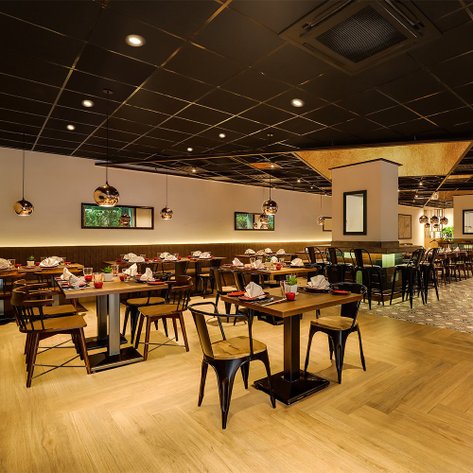 Ein modernes Restaurant mit eleganten Holztischen und Stühlen, dekoriert mit stilvollen Pendelleuchten und Pflanzen.