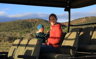 Mutter und Kind genießen gemeinsam die Safari im offenen Jeep und lächeln in die Kamera – Garden Route Reise mit Kindern