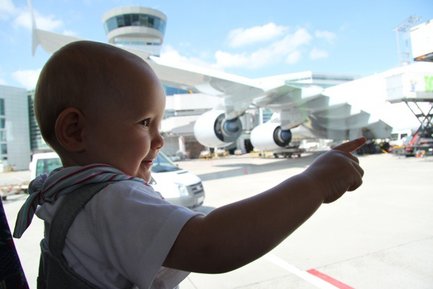 Ein kleines Kind zeigt begeistert auf ein großes Flugzeug, das am Flughafen geparkt ist, während die Sonne scheint.