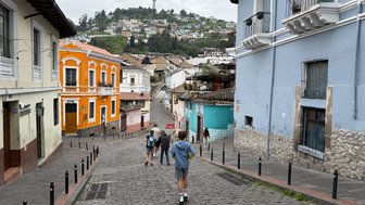 Eine Gruppe von Menschen geht eine steile, gepflasterte Straße hinunter, umgeben von bunten Häusern und Hügeln.