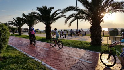 Zwei Kinder fahren auf Fahrrädern entlang einer palmengesäumten Promenade bei Sonnenuntergang in Batumi.