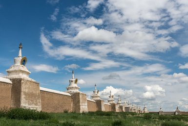 Eine lange Mauer mit weißen Stupas erstreckt sich unter einem strahlend blauen Himmel mit vielen Wolken.