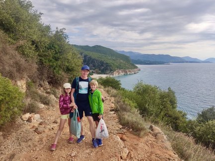 Ein Vater steht mit seinen zwei Kindern auf einem Wanderweg, umgeben von üppigem Grün und Blick auf das Meer.