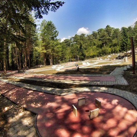 Ein Minigolfplatz in einem Waldgebiet, umgeben von hohen Bäumen und einem klaren blauen Himmel.