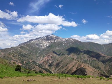 Die majestätischen Chimgan-Berge erheben sich unter einem strahlend blauen Himmel mit weißen Wolken und schneebedeckten Gipfeln.