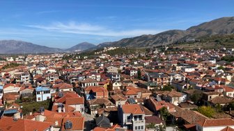 Eine weite Aussicht auf die Stadt Korça, mit zahlreichen Häusern und roten Dächern, umgeben von sanften Hügeln.