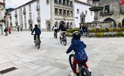 Eine Gruppe von Radfahrern, darunter ein Kind, fährt durch einen historischen Platz mit schönen Gebäuden im Hintergrund.
